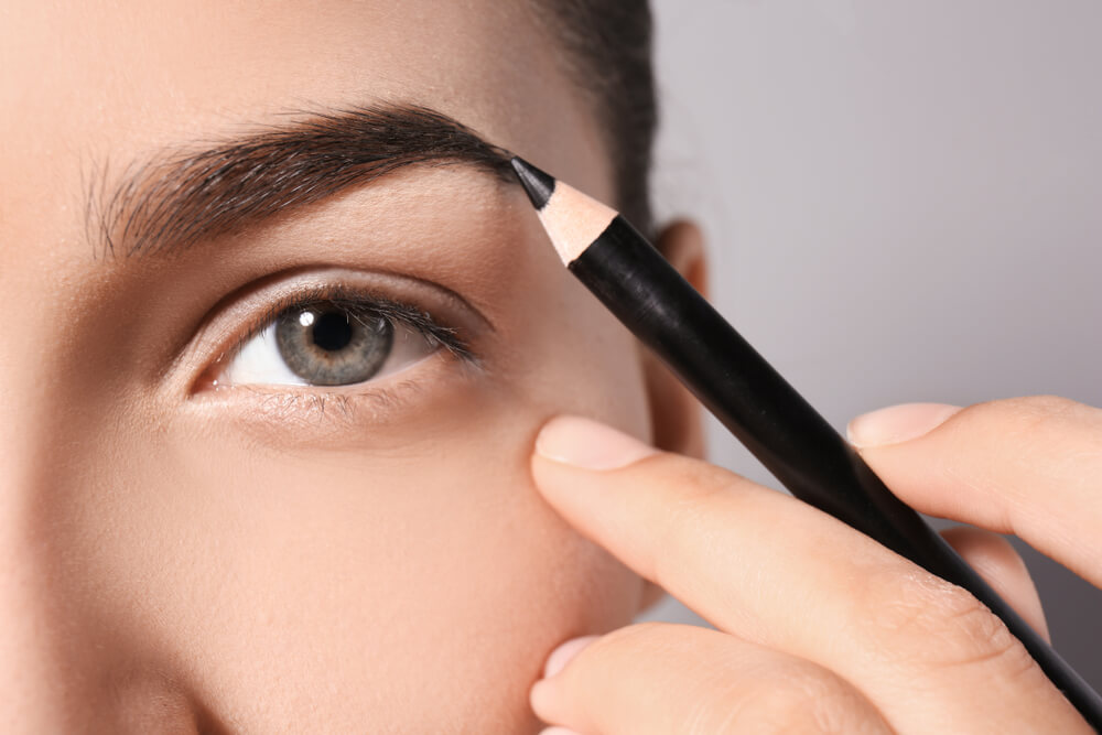 young woman correcting eyebrow shape with pencil